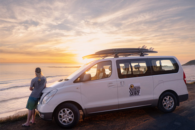 Stoked Surf Van standing next to the road with a sunrise in the background.
